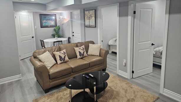A modern living room with a brown leather sofa, a glass coffee table, and a dining area with a white table and chairs. - Cozy 2 Bedrm with separate entrance
 (Kitchener)