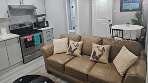 A modern kitchen with stainless steel appliances, a dining area with a round table and chairs, and a leather sofa with butterfly pillows. - Cozy 2 Bedrm with separate entrance
 (Kitchener)