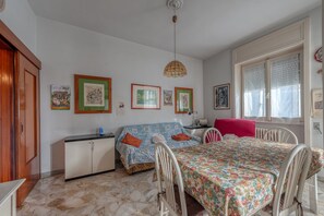 Een kamer met een bed, een bureau, een stoel, een raam met zonwering en kunstwerken aan de muur.