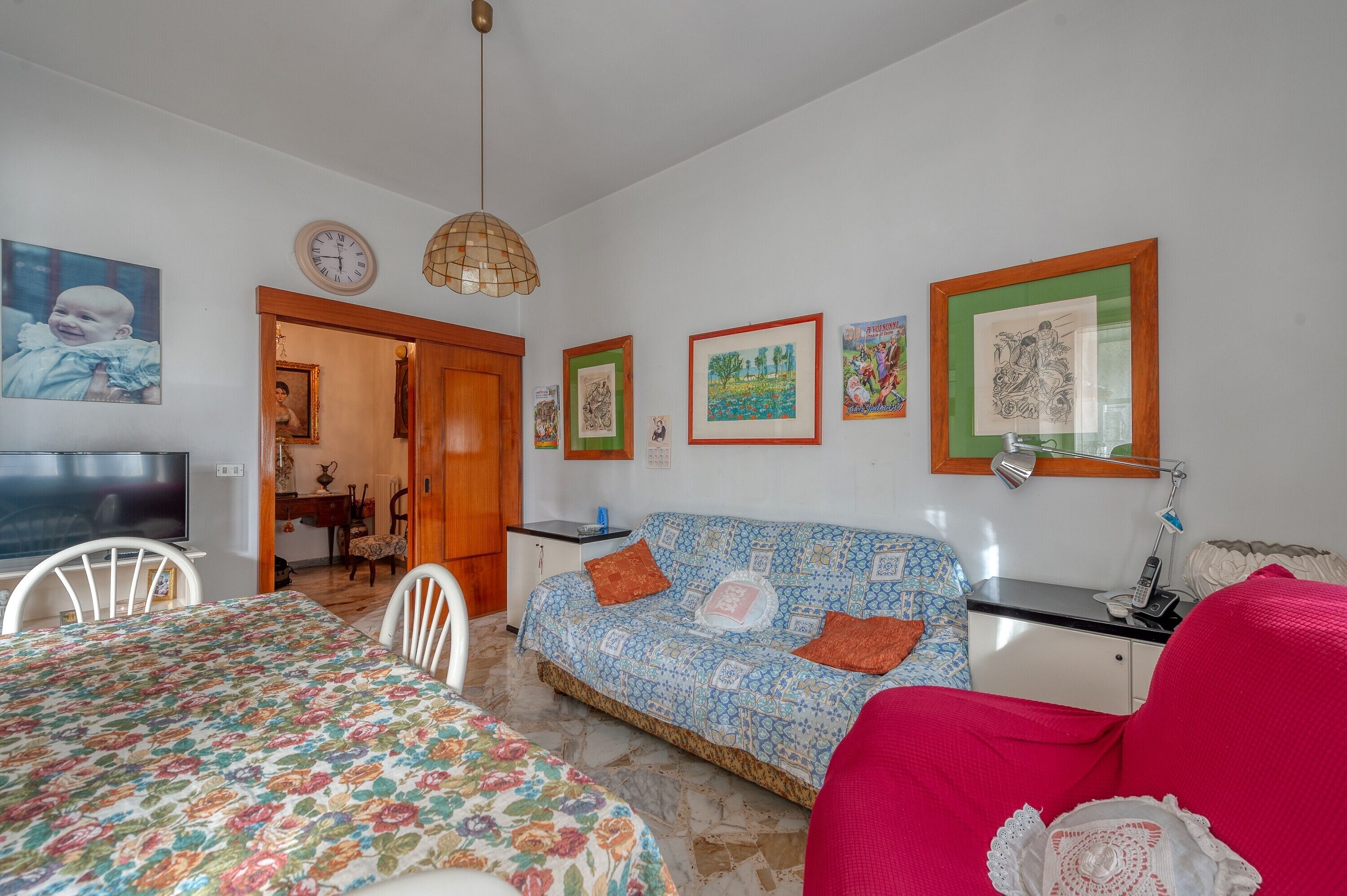 A room with a sofa, a dining table, a TV, and artwork on the walls.