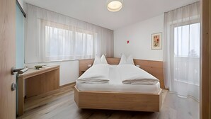 A bedroom with a wooden bed, a bedside table, a window with sheer curtains, and a ceiling light. - Holiday Apartment 'Appartement Wieser A' with Mountain View, Shared Garden and Wi-Fi (Schenna)