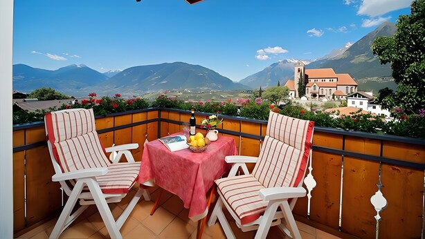 A balcony with two striped chairs, a table with a red tablecloth, and a bottle of wine. - Holiday Apartment 'Appartement Wieser A' with Mountain View, Shared Garden and Wi-Fi (Schenna)