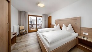 Habitación de hotel con una cama de madera, un escritorio, una silla y vistas al exterior.