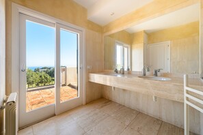 A modern bathroom with a large mirror, two sinks, and a view through the door. - Villa 'Can Roca' with Sea Views, Wi-Fi and Air Conditioning (Illes Balears)