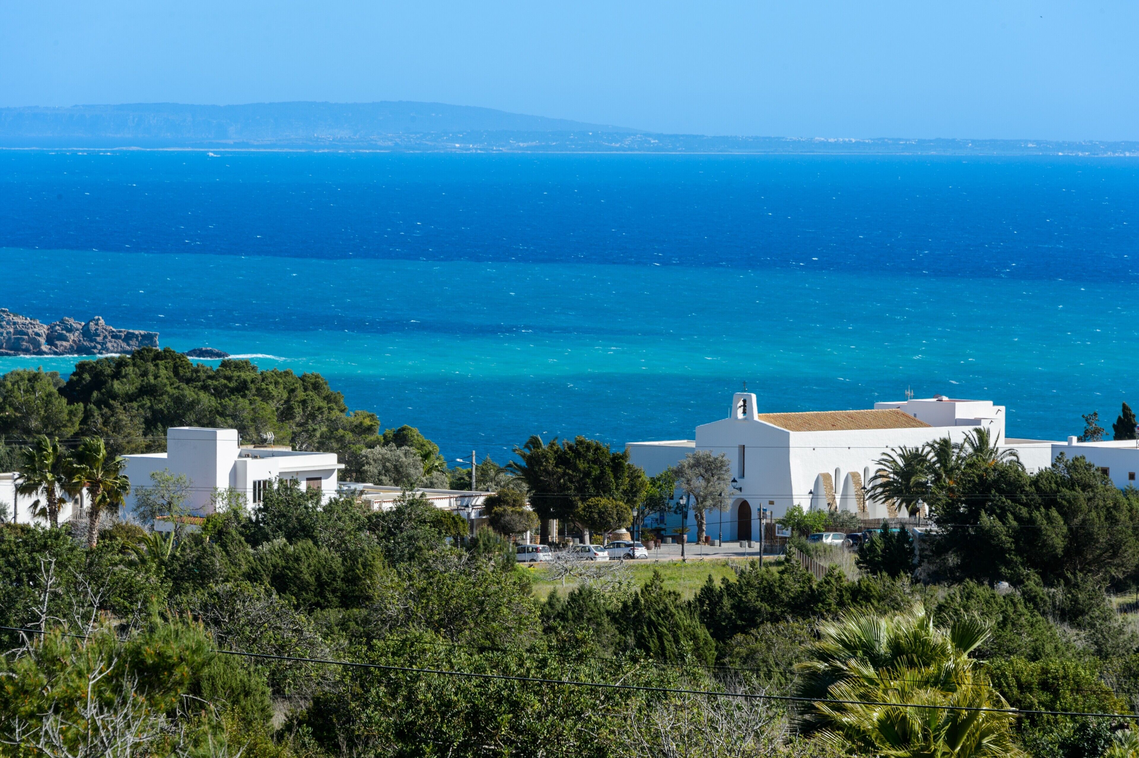 A coastal view with white buildings, a clear blue sea, and lush greenery.