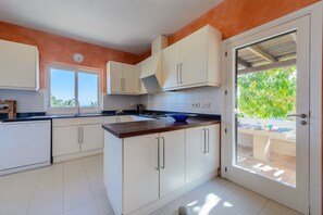 A modern kitchen with white cabinets, a wooden countertop, and a view of the outdoors through a glass door.