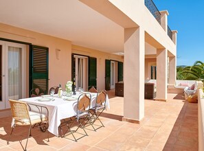 An outdoor dining area with a table set for four, surrounded by wicker chairs, and a balcony with a view of palm trees.