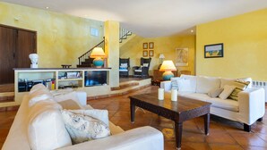A living room with a white sofa, a coffee table, and a TV. There is a staircase leading to another level. - Villa 'Can Roca' with Sea Views, Wi-Fi and Air Conditioning (Illes Balears)