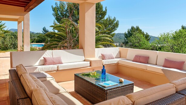 A covered outdoor seating area with sofas and a coffee table, overlooking a pool and greenery. - Villa 'Can Roca' with Sea Views, Wi-Fi and Air Conditioning (Illes Balears)