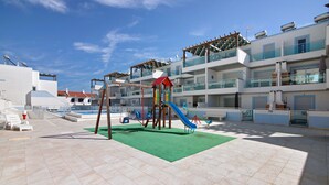 A children's play area with a slide and swings, a green mat, and a poolside lounge area with sun loungers. - Apartment 'Numar Residence Aa' with Shared Pool, Wi-Fi and Air Conditioning (Vila Nova de Cacela)