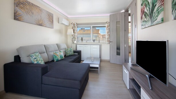 A modern living room with a sectional sofa, a flat-screen TV, a dining area, and a view of the outside. - Apartment 'Numar Residence Aa' with Shared Pool, Wi-Fi and Air Conditioning (Vila Nova de Cacela)