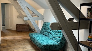A loft-style room with a wooden floor, a teal patterned sofa, a staircase, and a bookshelf.