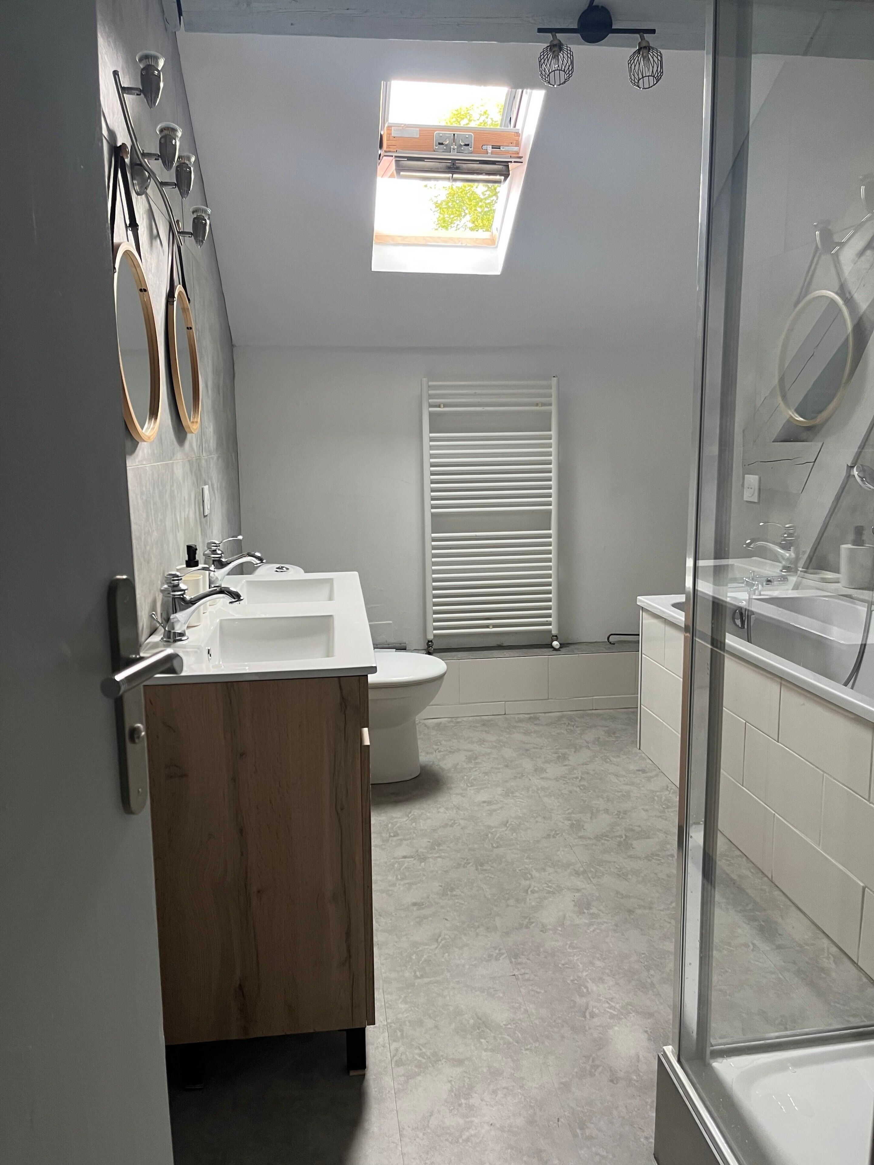 Ein modernes Badezimmer mit Oberlicht, einer freistehenden Badewanne und einem Holzlagerfläschchen.