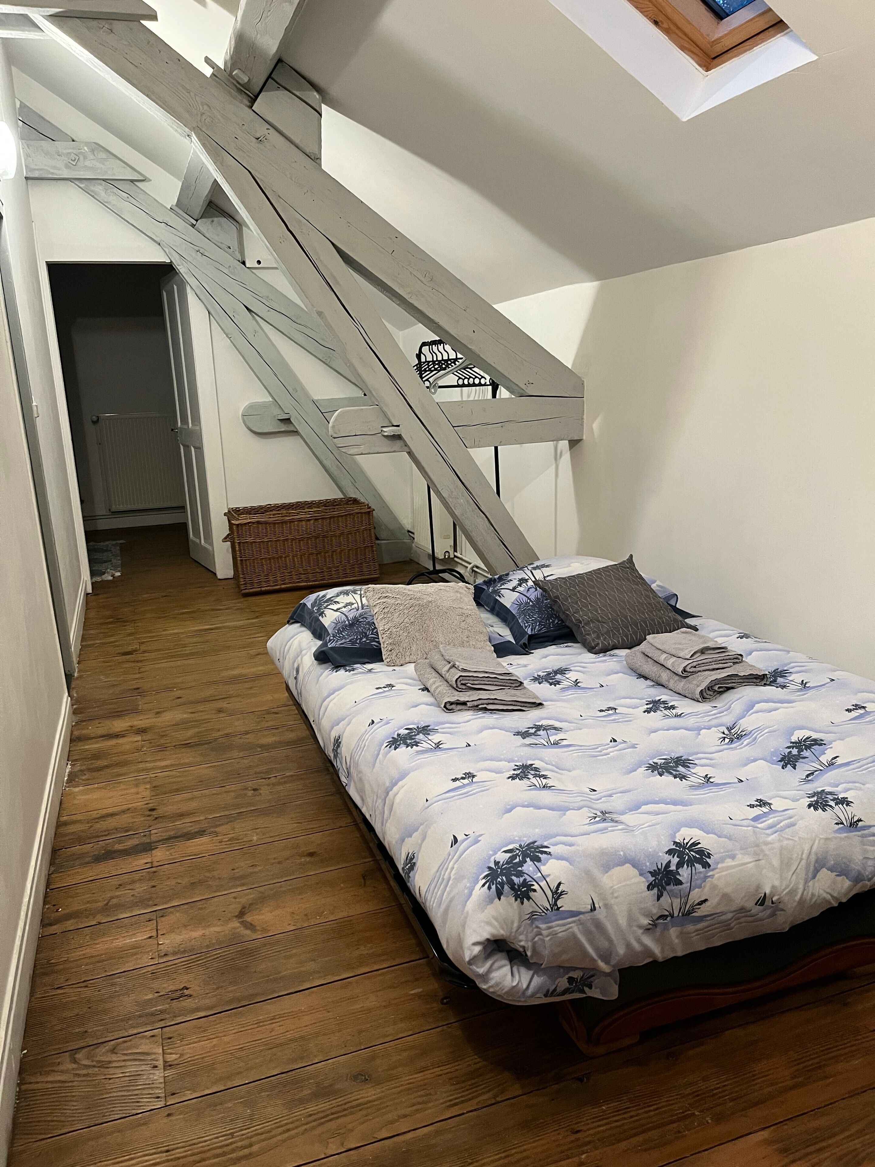 A bedroom with a wooden floor, a bed with a floral bedspread, a wooden ladder, and a small window.