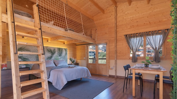 Een houten interieur met een bed, een eettafel en een ladder.