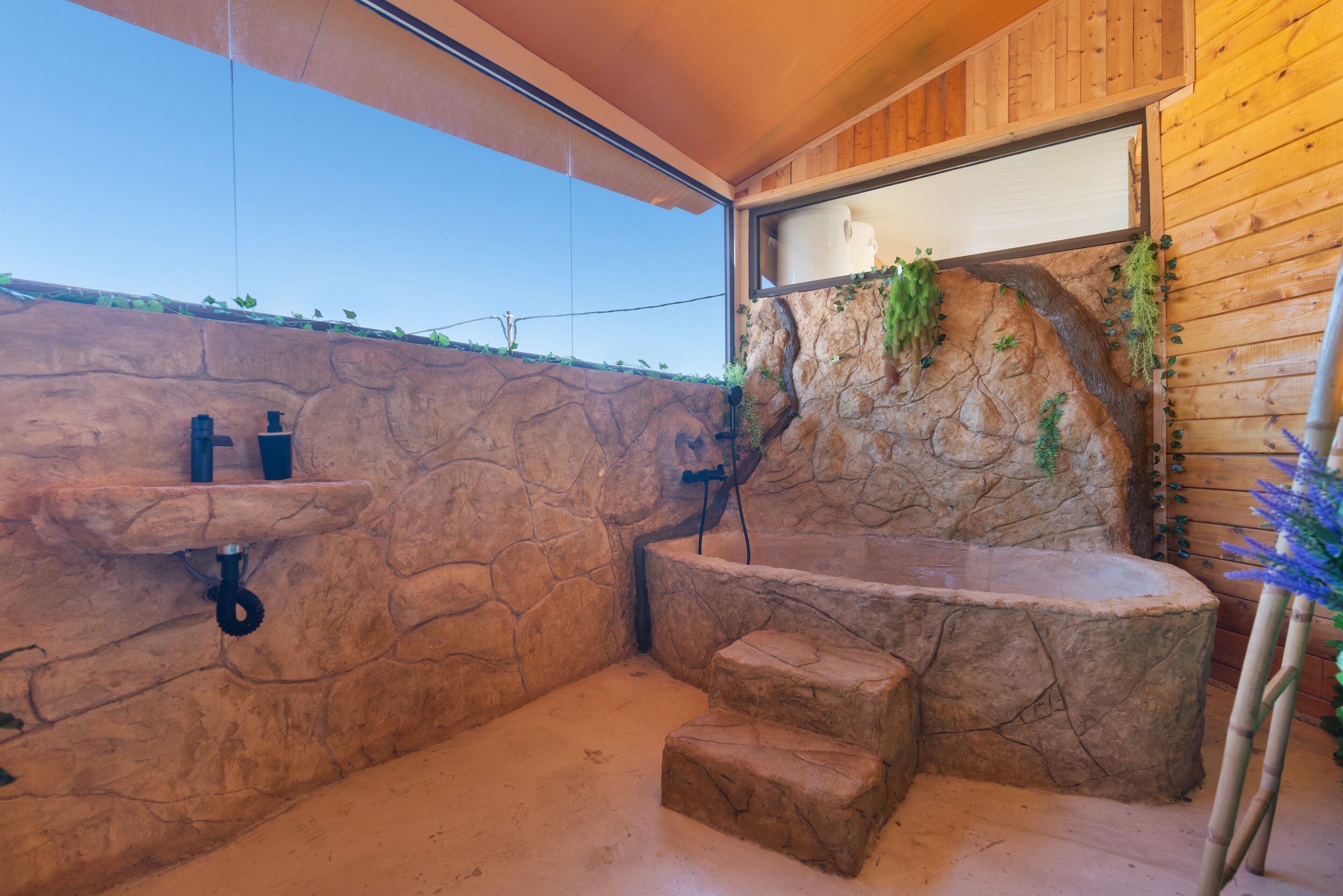 A stone-walled bathroom with a bathtub, a shower, and a window overlooking a natural landscape.