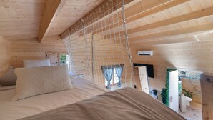 Een slaapkamer in een houten blokhut met een bed, een hangmat en uitzicht op de omgeving.