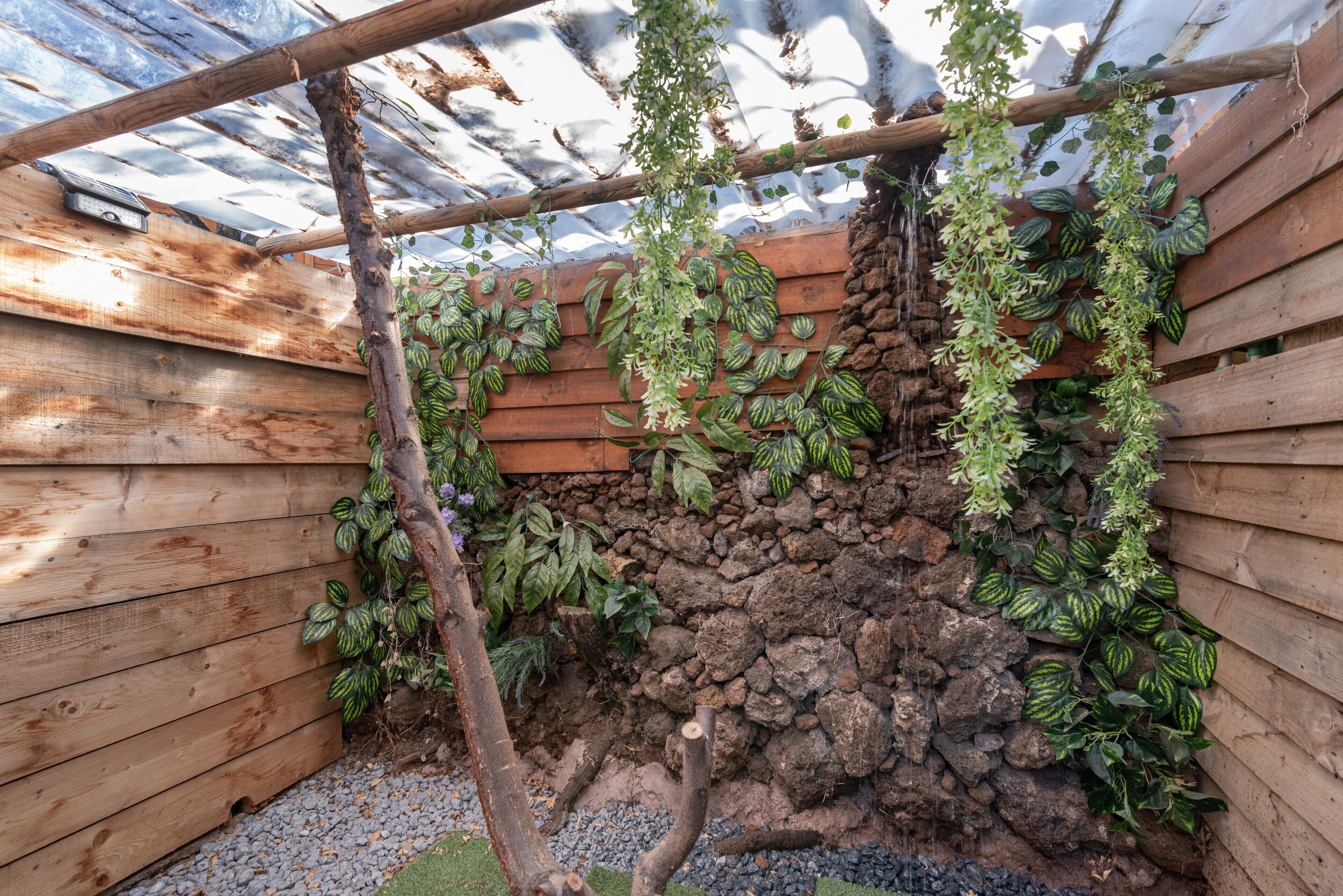 Une structure en bois recouverte de plantes grimpantes, un mur en pierre et un plancher en bois.