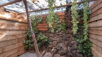 Une structure en bois recouverte de plantes grimpantes, un mur en pierre et un plancher en bois.