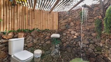 A stone wall with a waterfall feature, a toilet, and a bamboo pergola.