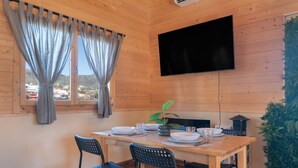 Een kamer met houten lambrisering, een eettafel gedekt voor vier personen, een flatscreen televisie aan de muur en een raam met gordijnen.