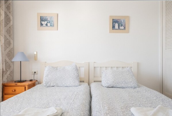 Un lit double avec une tête de lit en bois, deux oreillers, une table de chevet avec une lampe, et deux œuvres d’art encadrées accrochées au mur.