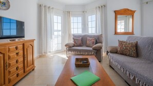 A living room with a sofa, armchair, wooden cabinet, television, and a mirror. - Apartment 'Flat3-5 Chaparil Beach' with Sea View, Wi-Fi and Air Conditioning (Nerja)