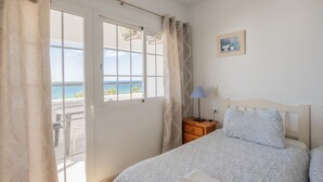 A bedroom with a bed, a nightstand, a lamp, a window with curtains, and a painting on the wall. - Apartment 'Flat3-5 Chaparil Beach' with Sea View, Wi-Fi and Air Conditioning (Nerja)