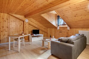 A wooden interior with a loft bedroom, a sofa, a table, and a TV.