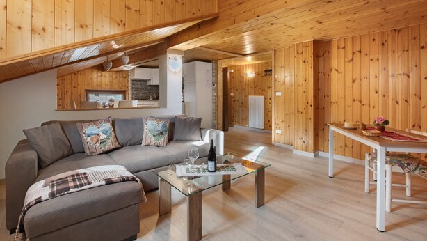 Ein gemütliches Wohnzimmer mit Sofa, Couchtisch und Esstisch, Holzwänden und einer Küche im Hintergrund.