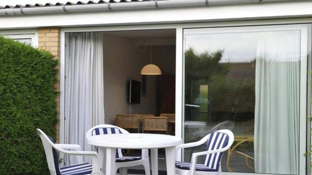A patio with a round table and four chairs, a sliding glass door, and a TV mounted on the wall. - 3 Person Holiday Home in Nexo (Nexø)