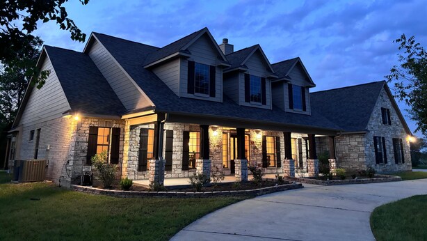A two-story house with a stone facade, multiple windows, and a driveway.