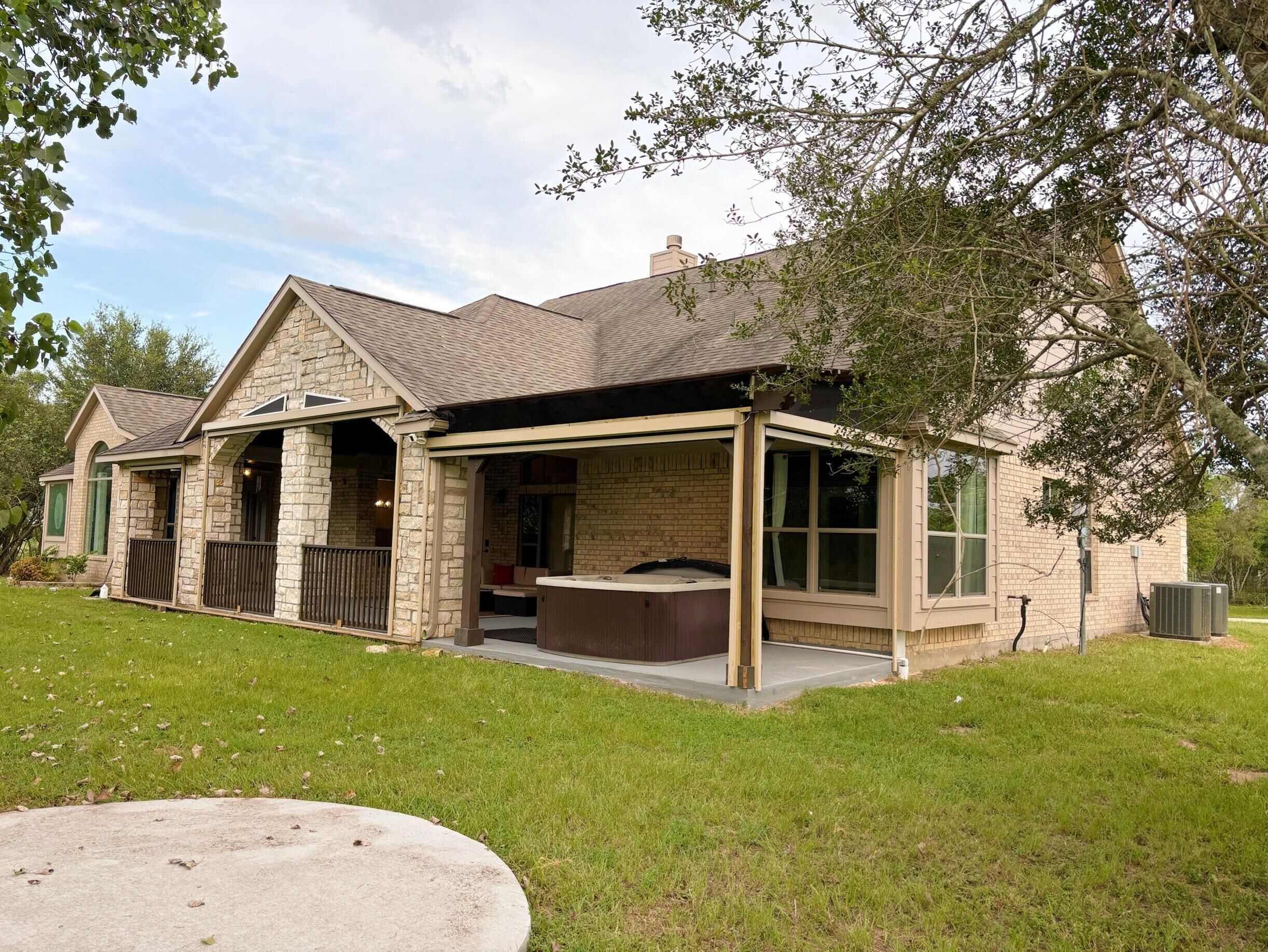 A two-story stone house with a covered patio and a hot tub.