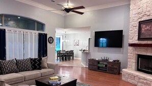 A living room with a sofa, coffee table, and fireplace. There is a TV mounted on the wall and a ceiling fan.