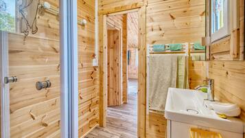 A wooden interior with a bathroom featuring a sink, mirror, and towel rack.