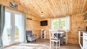 Et interiør af en træhytte med et spiseområde, en sofa, et fjernsyn og en bogreol.