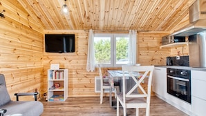 Et trægulv med en sofa, spisebord, stole, et fjernsyn og et køkken.