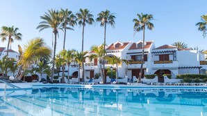 A resort with a swimming pool, palm trees, and white buildings with red roofs.