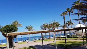 A coastal park with a pergola, palm trees, and a view of the sea.