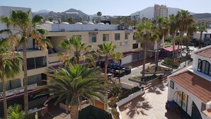 A multi-story building with outdoor seating areas, palm trees, and a view of a mountain in the background.