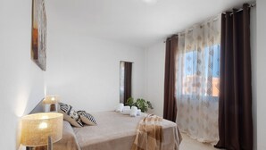 Ein Schlafzimmer mit Bett, Nachttischlampe, Spiegel, Pflanze und Vorhängen.