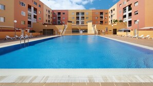 Ein Schwimmbecken mit Liegestühlen und ein mehrstöckiges Gebäude mit Balkonen.