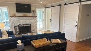 A living room with a fireplace, dark blue sofas, a coffee table, and a sliding door. - Country BEACH home! (Southold)