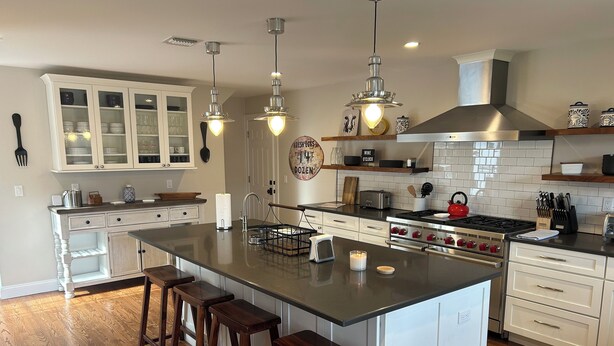 A modern kitchen with a large island, bar stools, stainless steel appliances, and white cabinetry. - Country BEACH home! (Southold)