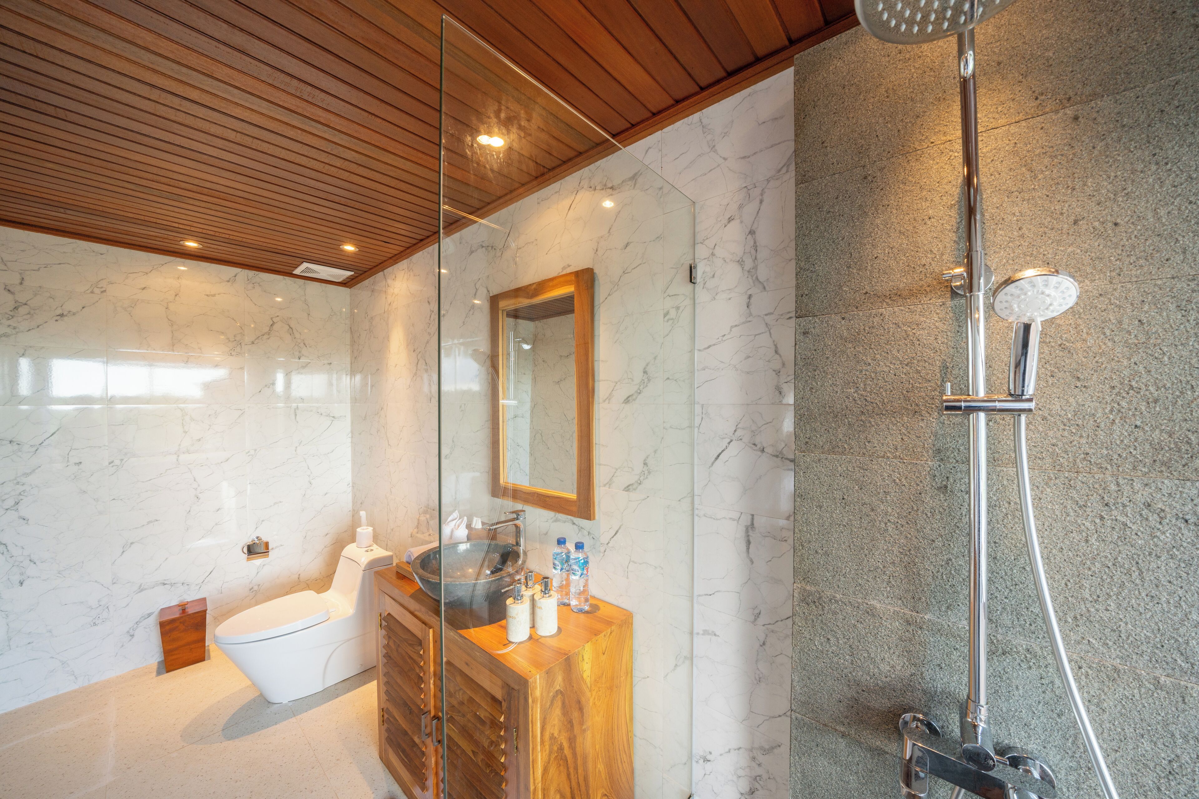 Ein modernes Badezimmer mit Marmorwand, Holzwaschtisch und einer Duschkabine aus Glas.