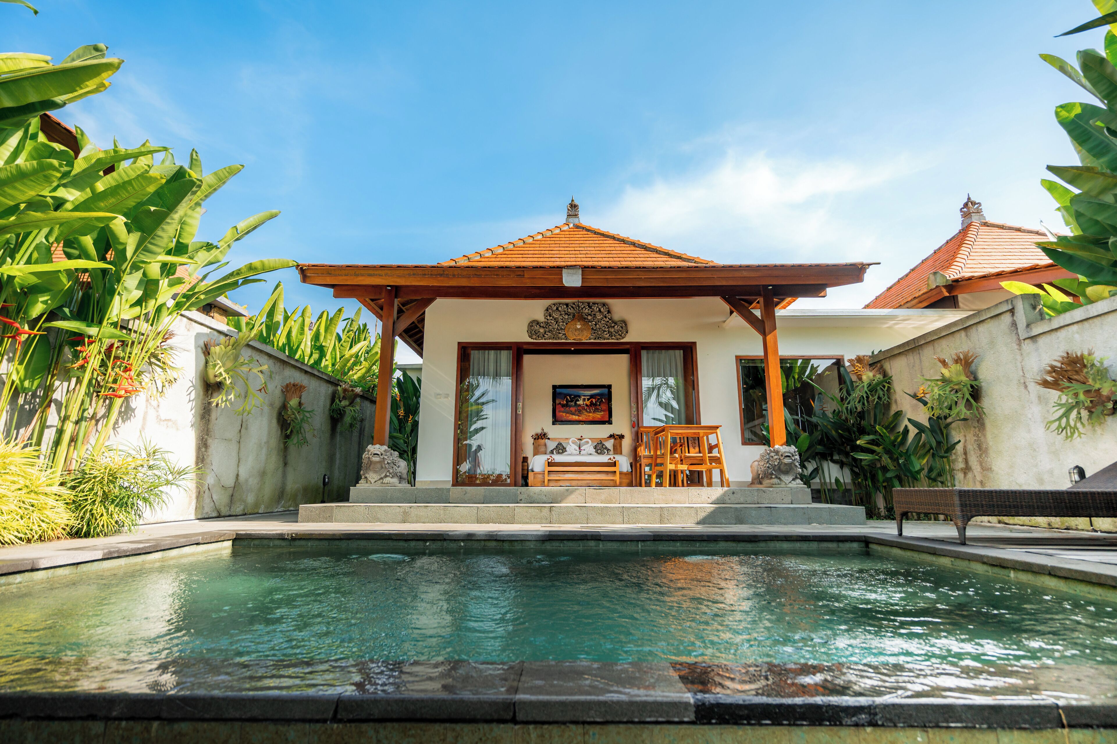 A pool area with a covered seating area, a statue, and lush greenery.