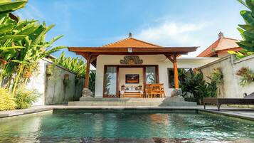 A pool area with a covered seating area, a statue, and lush greenery.