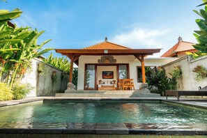 A pool area with a covered seating area, a statue, and lush greenery. - Kaki Uma Villa (Sebatu)