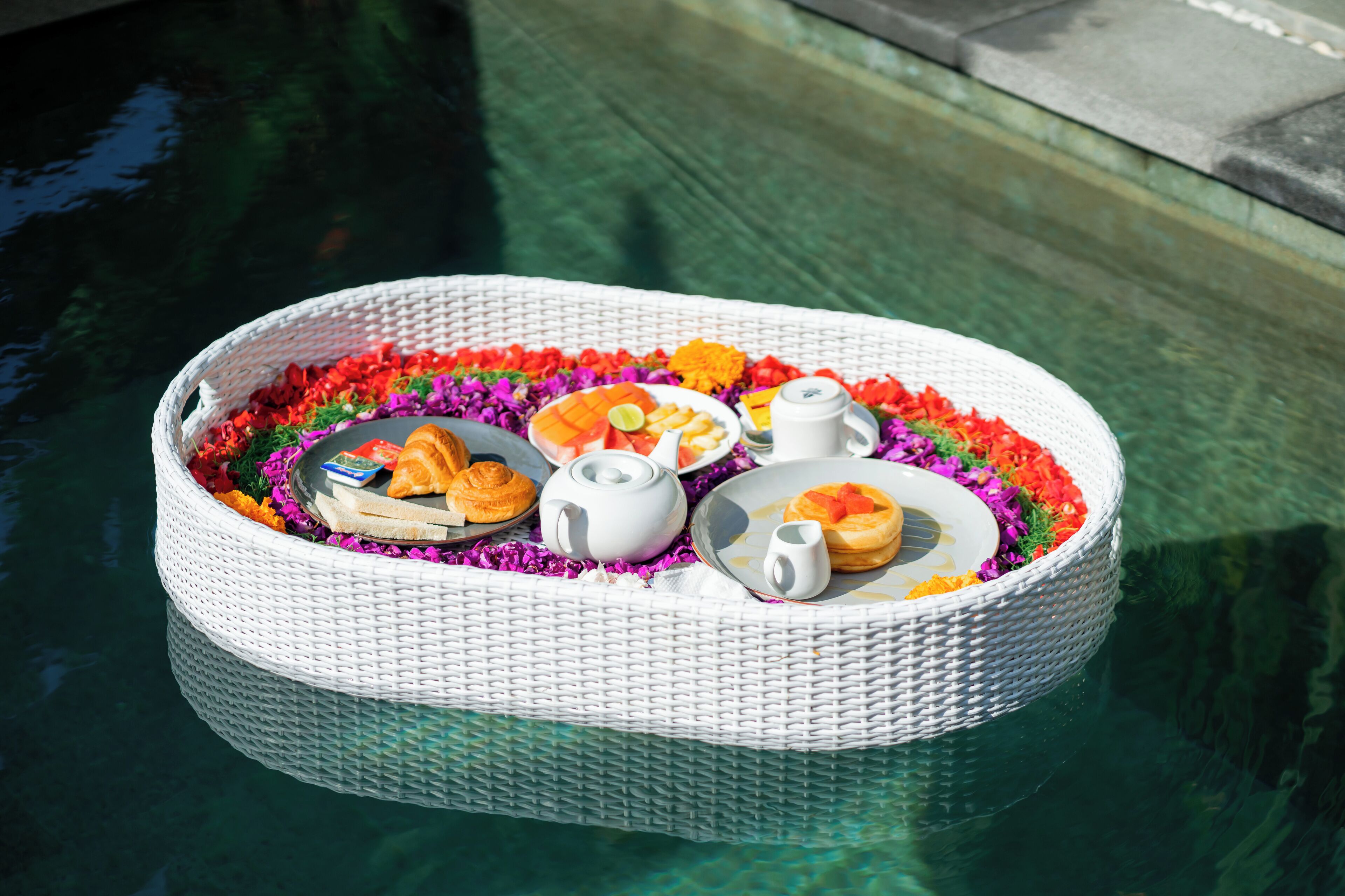 A floating wicker tray with food and drinks on a pool.