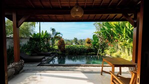 A covered outdoor area with a pool, wooden furniture, and lush tropical plants. - Kaki Uma Villa (Sebatu)